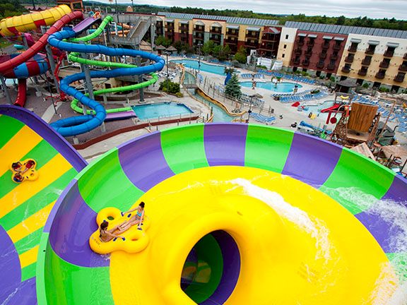 Sunny resort water park with colorful slides, a giant yellow splash pool, and people enjoying the rides.