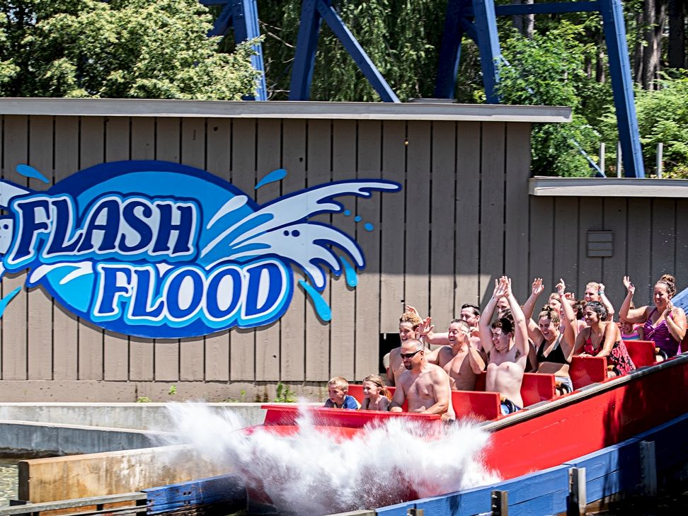 A red ride boat splashes through a watery attraction with &ldquo;Flash Flood&rdquo; graffiti and cheering riders in the front.