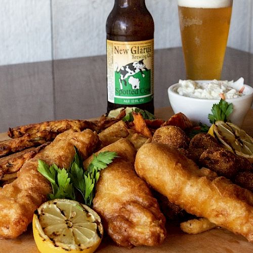 A meal with fried fish, lemon, fries, coleslaw, parsley garnish, a beer bottle, and a filled beer glass on a table setting.