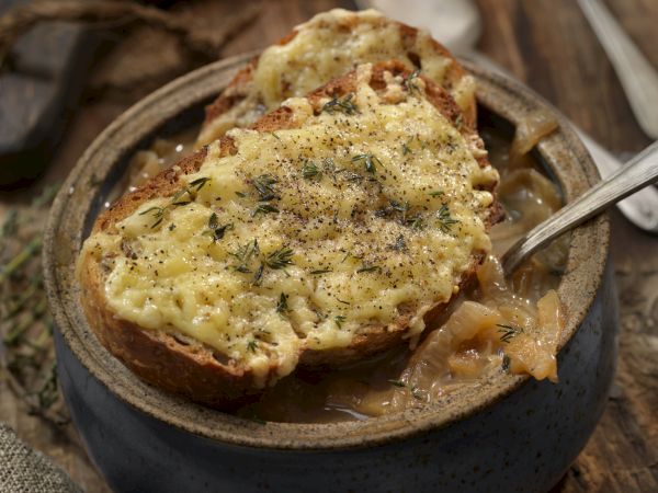 A rustic bowl of creamy mushroom soup topped with melted cheese and herbs, served with crusty bread on the side.