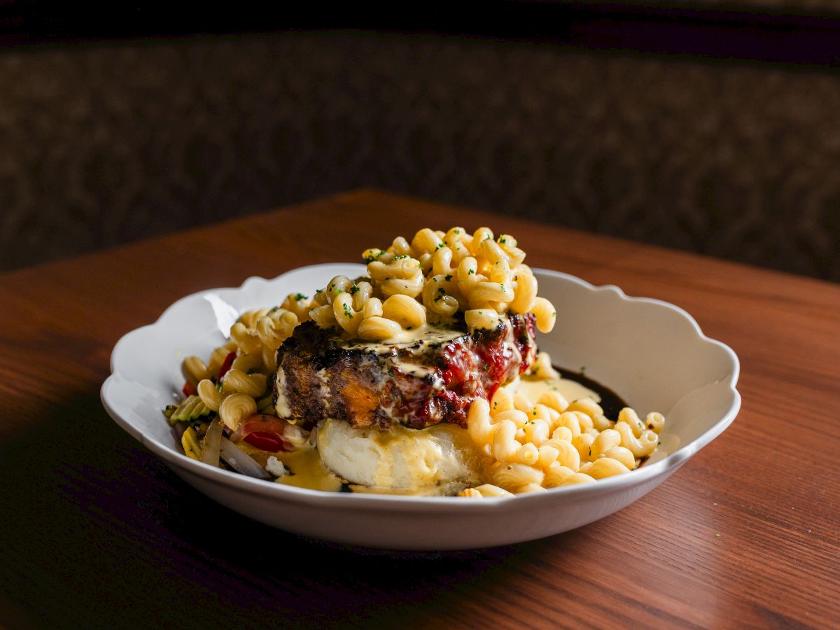 A plated dessert with a slice of cake topped with berries and nuts, alongside a swirl of cream and a side of crois&eacute;e macaroni-like topping.