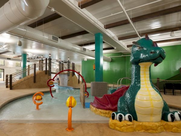 A colorful indoor water park with a small pool, slide, dragon-shaped inflatable float, and kid-friendly play features under bright lights. ends with period