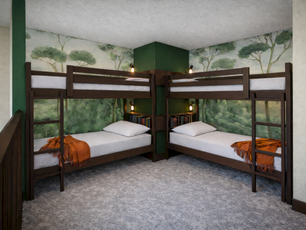 Two sets of dark wood bunk beds form a corner in a small, playful room with green tree mural walls and cozy orange blankets.