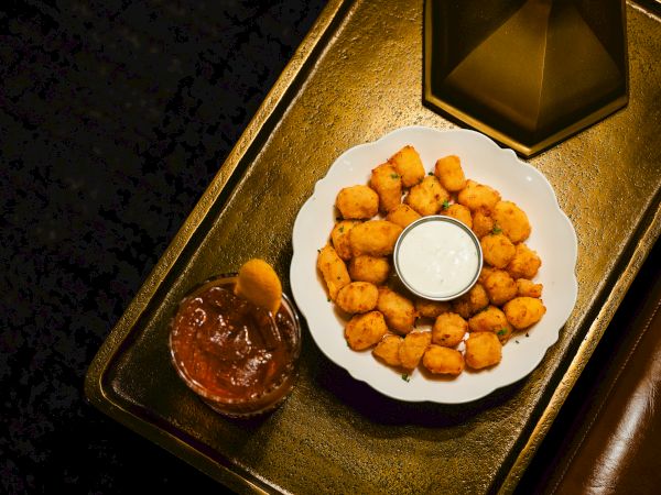 A plate of golden fried bites with a white dipping sauce and a side of red sauce on a tray.