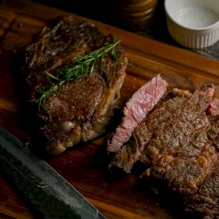 Grilled steak sliced over a dark plate with a green bean garnish, glossy sauce, and a subtle charred crust.