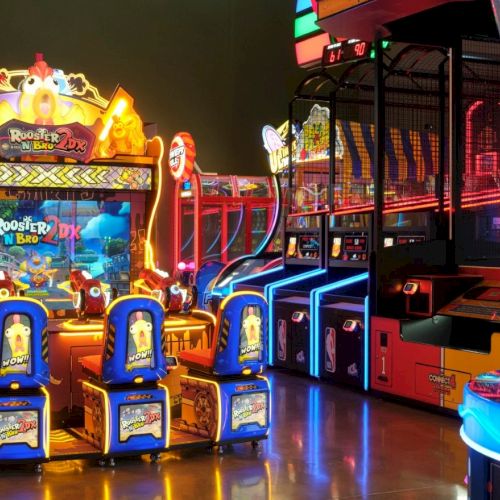 Colorful arcade games and prize machines line a lit-up indoor arcade, with bright neon elements and playful character graphics, inviting play.