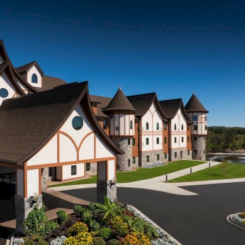 University-style lodge with Tudor-style fa&ccedil;ades, sloped roofs, and a circular driveway set against blue skies and manicured grounds.