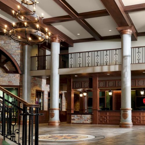 A grand hotel lobby with stone arches, wooden beams, marble columns, a circular chandelier, and a front desk area on the right, elegant and spacious.
