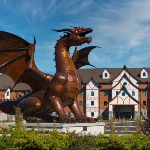 A large bronze dragon statue in front of a themed building complex, perched on a pedestal with wings spread open. is that.