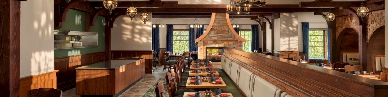 A stylish restaurant interior with wooden beams, warm lighting, long dining tables set with plates, glasses, and napkins, and a cozy, inviting atmosphere.