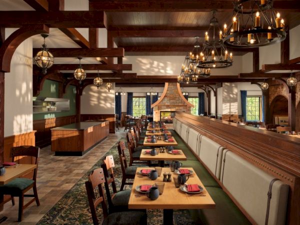 A stylish restaurant with warm wooden beams, long dining tables, leather chairs, chandeliers, and cozy booths along a bright, airy space.