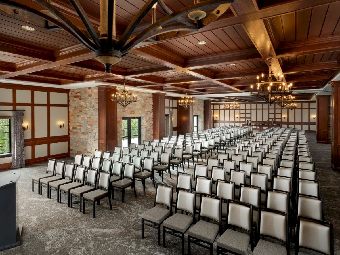 A spacious, wood-ceiling hall set up with rows of upholstered chairs and chandeliers for an event.