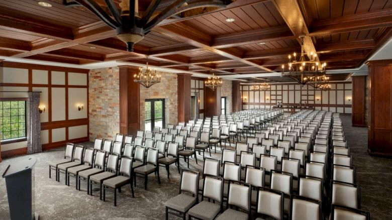 A spacious, wood-ceiling hall set up with rows of upholstered chairs and chandeliers for an event.