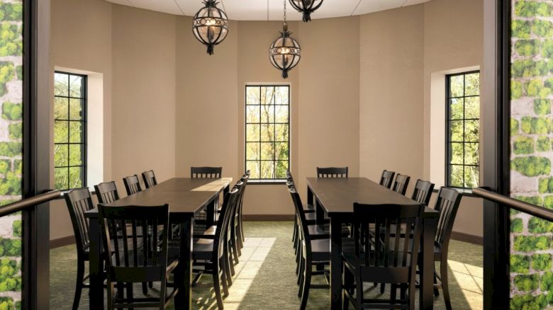 A bright dining room with two long dark tables, multiple black chairs, and three modern pendant lights hanging from a beige ceiling.