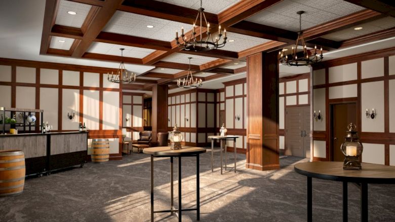 A rustic-style interior with wood paneled walls, chandeliers, high tables, and a bar area, resembling a spacious old-time saloon or tavern.