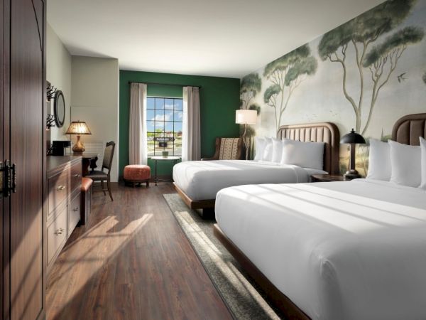 Two large beds in a stylish hotel room with a forest mural, wooden floor, green accent wall, seating by the window, and soft lighting.