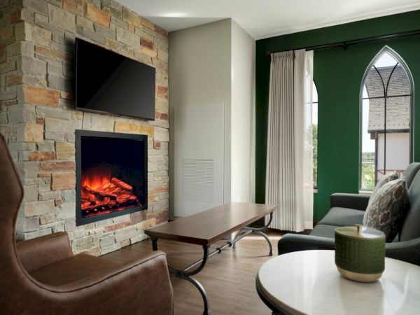 Cozy living room with a stone fireplace, mounted TV, brown seating, a coffee table, and a green door/arched window adding charm, inviting warmth.