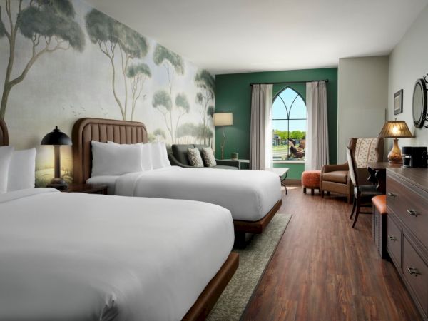 Two queen beds with white linens, a mural of trees on the wall, warm lamps, a seating area, and a doorway opening to a balcony with a view.