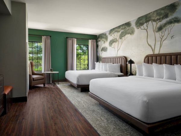 Two double beds in a stylish hotel room with a mural, wood floors, green walls, a seating area by a window, and a desk, bright and inviting.