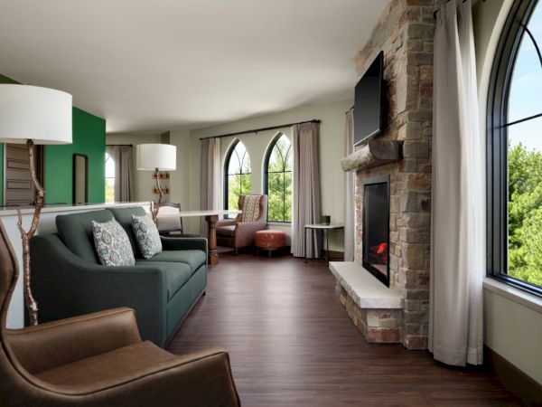 A modern living room with a stone fireplace, arched windows, green accent wall, and comfortable seating in a spacious, airy space.