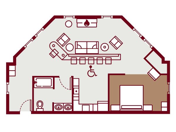 A floor plan of a living area with a curved outer wall, seating, desks, a kitchenette, bathroom, and a central accessibility area, ending with a period.