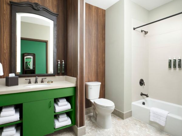A modern bathroom with a green vanity, open shelves, large mirror, toilet, and a glass-door shower; clean lines, neutral tones, and bright lighting.