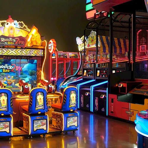 A colorful arcade with many lighted arcade games and racing/skill machines in a dimly lit entertainment center.