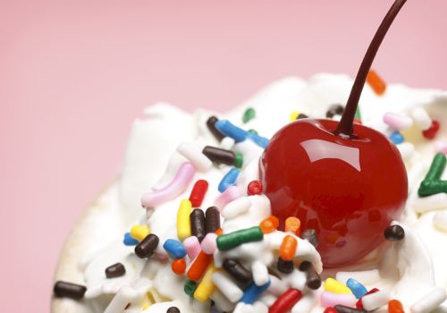 A red candy apple on crushed candy sprinkles, with colorful bits scattered around and a brown stick in view.