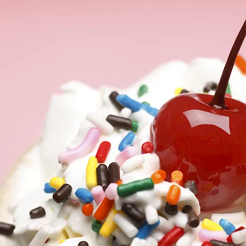A red candy apple on crushed candy sprinkles, with colorful bits scattered around and a brown stick in view.