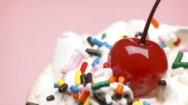 A red candy apple on crushed candy sprinkles, with colorful bits scattered around and a brown stick in view.