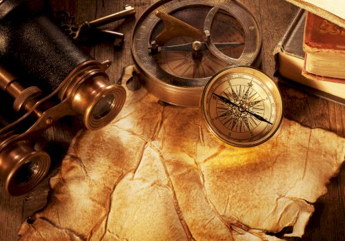 A gold compass and compass rose sit on an old parchment map, alongside a spyglass, nautical tools, and brass instruments for navigation.