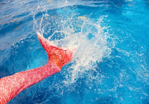 A swimmer in the water splashes hard, with a red body suit breaking the surface during a fast stroke.