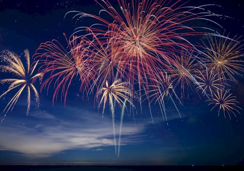 Colorful fireworks burst across a night sky, with red, gold, and white trails lighting up the clouds.