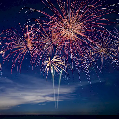 Colorful fireworks burst across a night sky, with red, gold, and white trails lighting up the clouds.