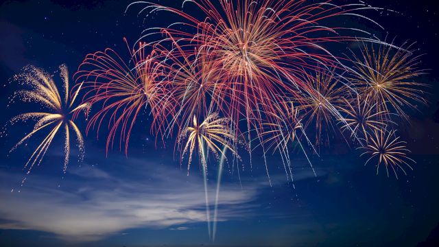 Colorful fireworks burst across a night sky, with red, gold, and white trails lighting up the clouds.