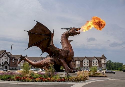 A giant cartoon-style dragon breathes fire over a landscaped hotel entrance with cars and buildings in the background.