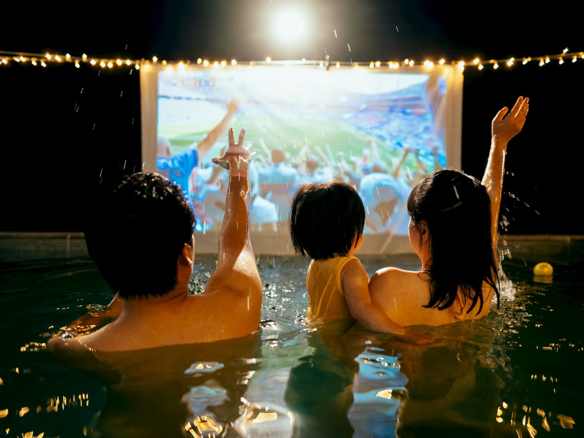 A crowd in the rain cheers at a concert stage with raised hands, sparks, and confetti filling the night.