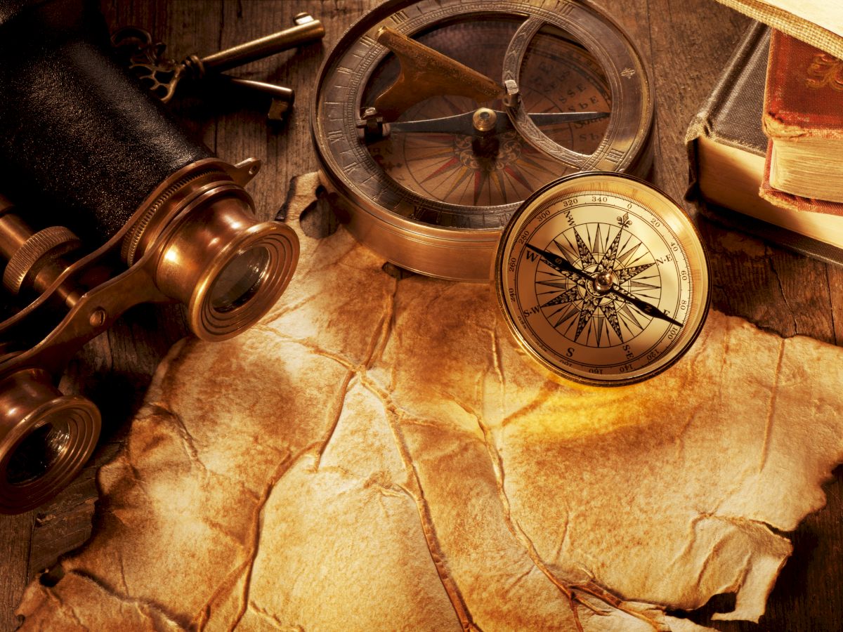 An antique compass and navigational instruments rest on old parchment maps and rolled scrolls, evoking treasure-hunting adventures.