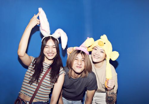 A group of friends pose with cute bunny and duck plush headbands on a blue backdrop, laughing together.