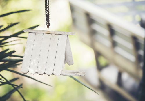 A small metal wind chime hangs in front of green plants, with rusted chain links swaying in the breeze.