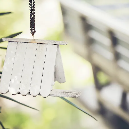 A small metal wind chime hangs in front of green plants, with rusted chain links swaying in the breeze.