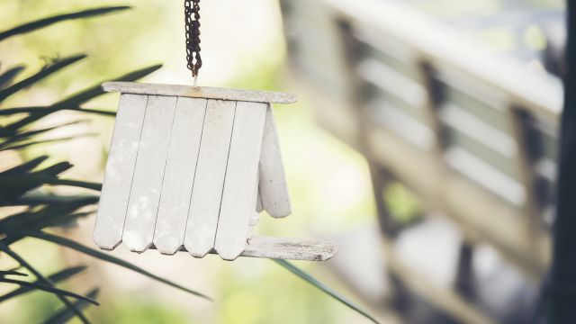 A small metal wind chime hangs in front of green plants, with rusted chain links swaying in the breeze.