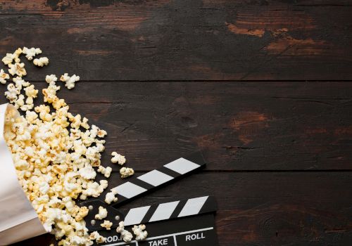 A film clapperboard and scattered popcorn sit on a dark wooden table, suggesting movie night or a cinema scene.