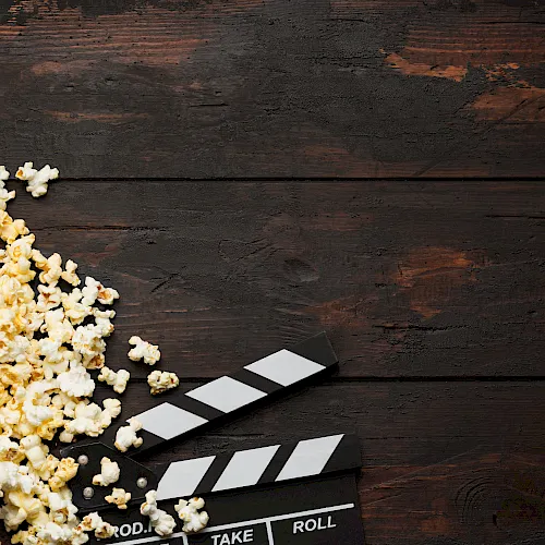 A film clapperboard and scattered popcorn sit on a dark wooden table, suggesting movie night or a cinema scene.
