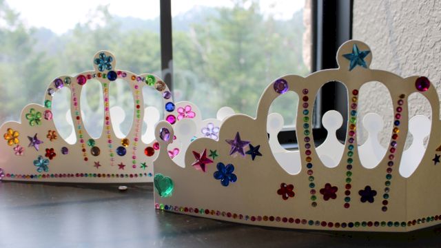 A pair of glittery gem-studded cardboard crowns with stars and colorful rhinestones sit by a window.