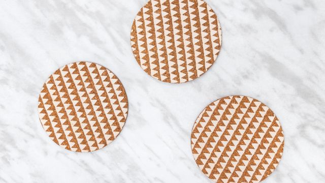 Three round patterned cork coasters with a zigzag motif sit on a light marble background.