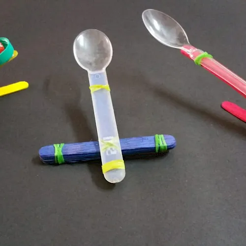 Three DIY maracas and shakers made from plastic spoons and bottle caps in bright yellow, blue, and red.