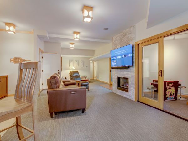 A bright home living room with brown leather sofas, a wall-mounted TV, a stone fireplace, and recessed ceiling lights.