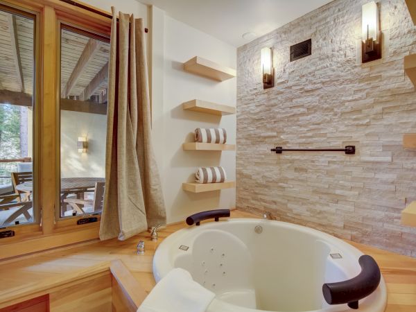 A bright bathroom with a jetted tub, stone-tile wall, wall-mounted lights, and neatly hung striped towels.