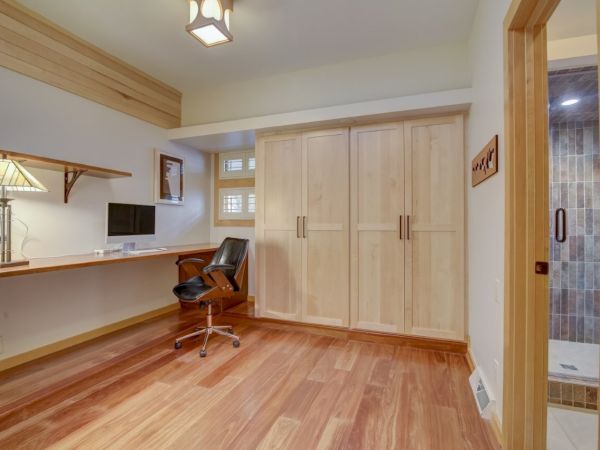 Bright modern office room with wooden built-in cabinets, a desk, barstool chair, and a doorway to a tiled bathroom.